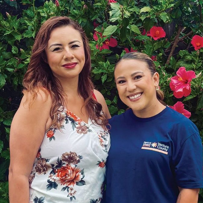 Rescue Mission Alliance staff members smiling outdoors with vibrant pink flowers in background.
