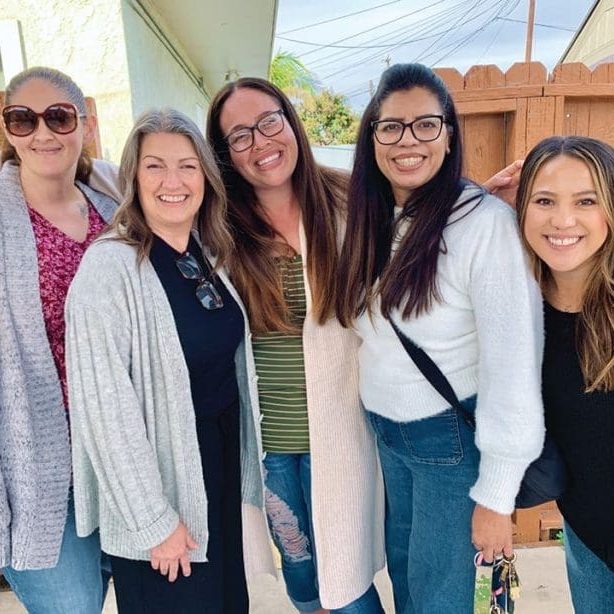 Five women standing together outdoors, smiling at the camera in front of a wooden fence on a sunny day—radiating faith and friendship, they embody the spirit that God isn't done with me yet.
