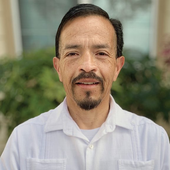 Rescue Mission Alliance volunteer smiling outdoors in front of greenery.