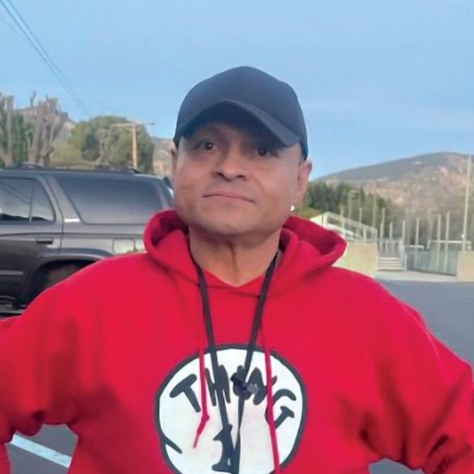 Rescue Mission volunteer in red hoodie and black cap outdoors in parking lot.