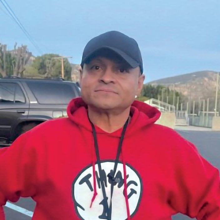 Rescue Mission volunteer in red hoodie and black cap outdoors in parking lot.