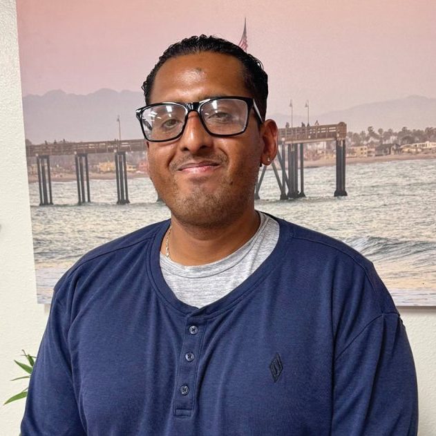 Rescue Mission volunteer smiling indoors with a waterfront mural in the background.