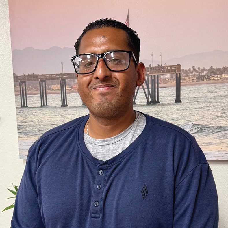 Rescue Mission volunteer smiling indoors with a waterfront mural in the background.