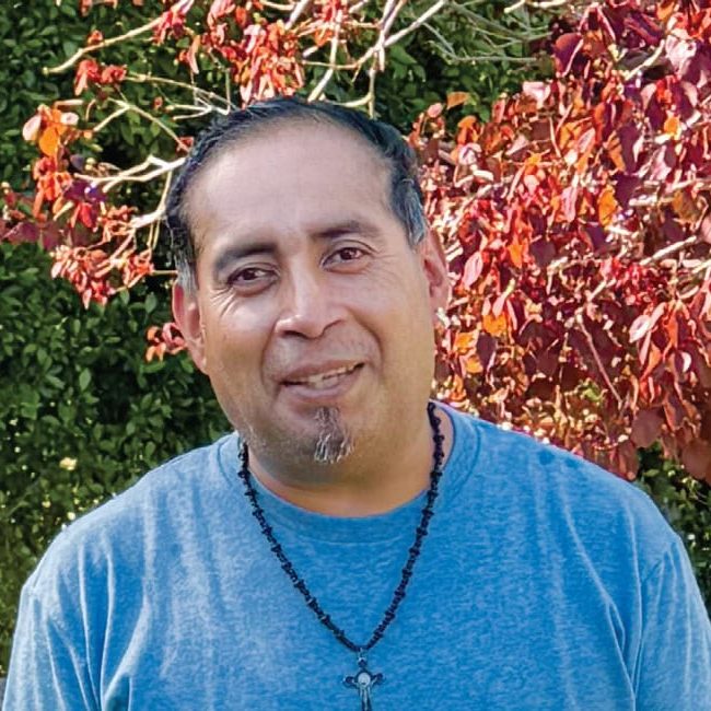 Rescue Mission Alliance volunteer smiling outdoors with colorful autumn leaves in background.