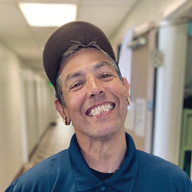 Smiling man in a blue polo shirt and cap at Rescue Mission Alliance facility.